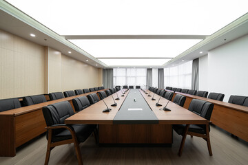  large conference room with a long wooden table, black chairs, microphones, and a bright ceiling light