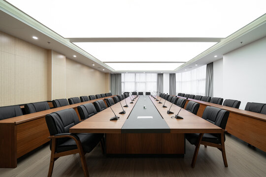  large conference room with a long wooden table, black chairs, microphones, and a bright ceiling light