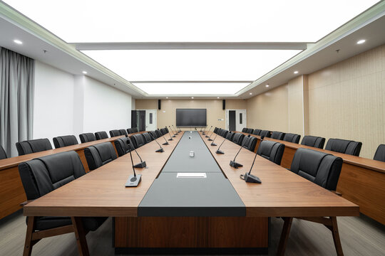  large conference room with a long wooden table, black chairs, microphones, and a bright ceiling light