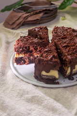 Chocolate carrot cake with cream cheese frosting, topped with chocolate ganache and sprinkled with shredded chocolate, placed on a white ceramic plate.