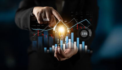 A business professional points at a glowing light bulb while analyzing financial data on digital...