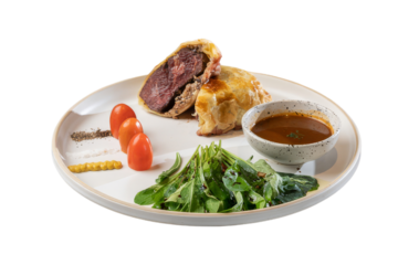 A delicious beef wellington with vegetables and sauce on plate, ready to be enjoyed. The dish includes tomatoes, arugula, and a savory sauce