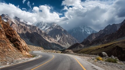 Naklejka premium Majestic Mountain Landscape with Winding Road Surrounded by Dramatic Peaks and Cloudy Sky in Scenic Natural Environment
