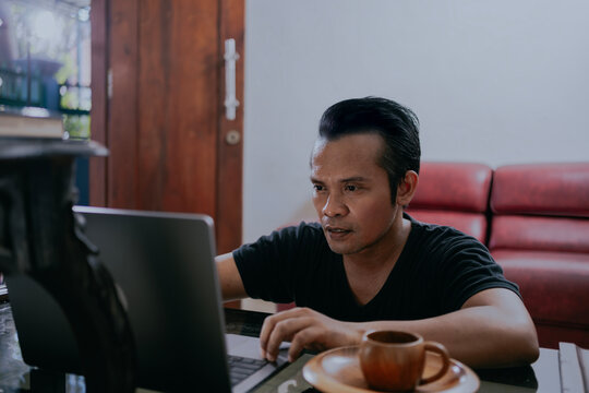 Young asian man using laptop sitting on the floor in living room enjoying content at home.