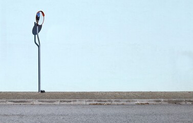 Traffic convex mirror on a pole with light blue plaster wall on behind. Sidewalk and street in front. Background for copy space.