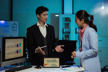 Financial analysts work overtime analyzing data on tablets, laptops, and graphs.