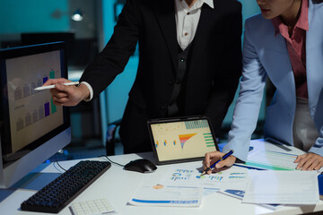 Financial analysts work overtime analyzing data on tablets, laptops, and graphs.