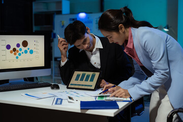 Financial analysts work overtime analyzing data on tablets, laptops, and graphs. Collaboration, teamwork, and planning.