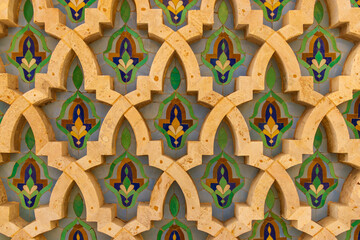 Traditional Islamic or Moroccan geometric wall pattern with green, blue, and gold details made of tiles and carved stone, ornamental background.