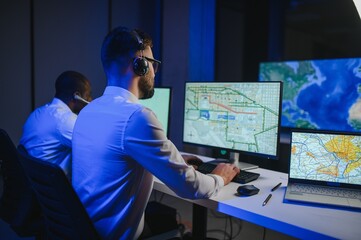 Male Data Scientist Works on Personal Computer Wearing a Headset in Big Infrastructure Control and Monitoring Room