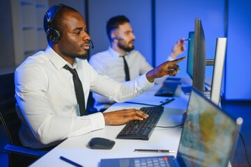 Center of dispatching maintenance. Portrait of men working via headset microphone while sitting on...