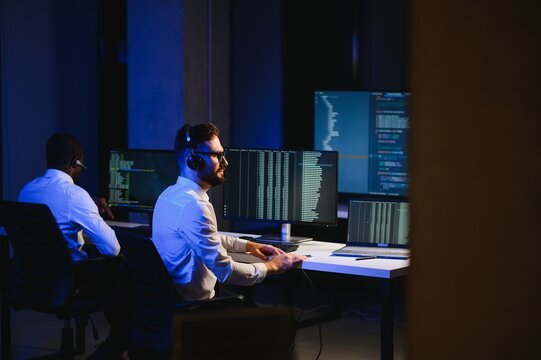 Male Data Scientist Works on Personal Computer Wearing a Headset in Big Infrastructure Control and Monitoring Room