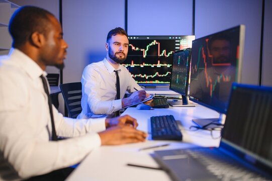 Two businessmen, financial analysts or investment advisers sitting at office desk with copmputers and documents