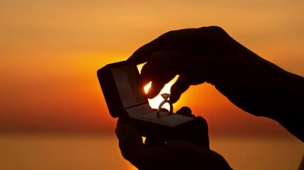 4k Close up silhouette male hands opening engagement ring box with diamond proposal ring on bright orange sunset background romantic marriage proposal moment love commitment emotional wedding concept - Powered by Adobe