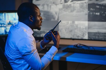 African-American security officer watching the screens talking on radio in control room