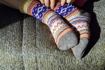Close-up of feet wearing woolen knitted socks lying on a sofa. Concept of winter wardrobe essentials, cold weather preparation, home insulation, cheerful indoor fashion, and practical comfort solution