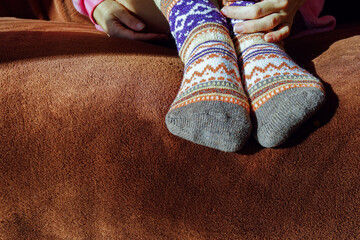 Person resting on a sofa wearing colorful geometric patterned socks. Symbolizes home relaxation, cozy clothing choice, weekend lifestyle, self-care moment, and appreciation of handcrafted textiles.