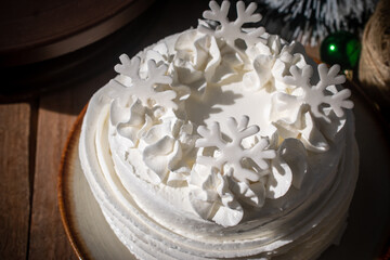 White buttercream cake decorated with snowflake toppers in a cozy Christmas and Happy New Year still life setting. The festive cake is placed on a rustic wooden table with warm light.