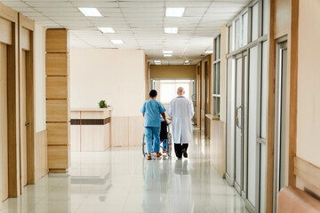 Two healthcare professionals escort a patient in a wheelchair down a bright, clean hospital corridor, reflecting care, safety, and support. © artitwpd
