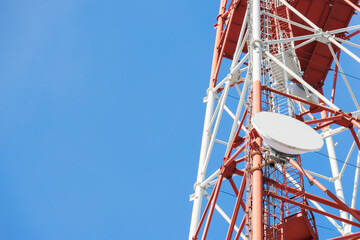A close-up view of a telecommunication tower with a satellite dish, set against a bright blue sky,...