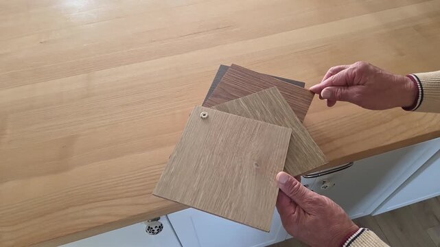 Main ouvrant un nuancier bois sur le plan de travail de la cuisine, choisir la couleur de son bois, d&eacute;coration int&eacute;rieure de la maison.
