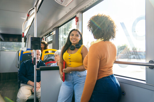 Young diverse women enjoying a conversation while traveling on a modern city bus, with other passengers in the background