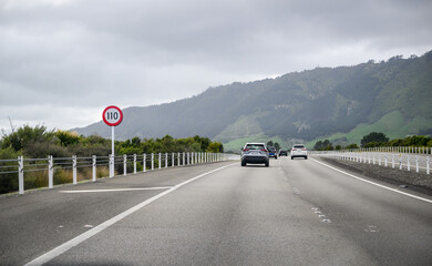 110 km/h speed limit sign at Kapiti Expressway. Cars travelling on the expressway under a cloudy sky. New Zealand;