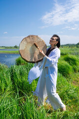 Female shaman in the white dress drumming outdoors