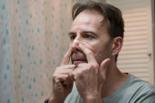 Man in the bathroom wearing anti snoring nasal strip breathing aid for better sleep quality.