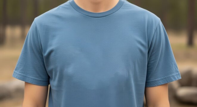 Close up of a man wearing a blue tshirt standing outside in nature with a blurred background of trees and rocks in the distance
