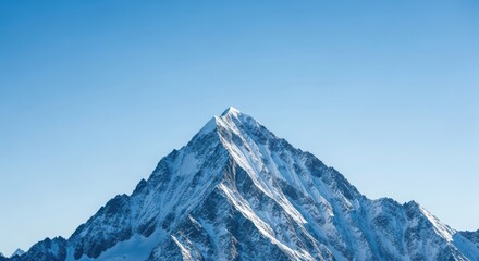 A snow capped mountain peak against a clear blue sky offers a stunning view of natures beauty and grandeur in the winter season