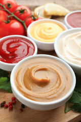 Different sauces in bowls and ingredients on wooden table, closeup