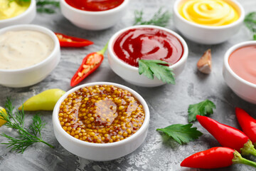 Different sauces in bowls and ingredients on grey textured table, closeup