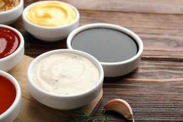Different sauces in bowls on wooden table, closeup