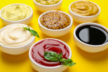 Different sauces and herbs on yellow background, closeup
