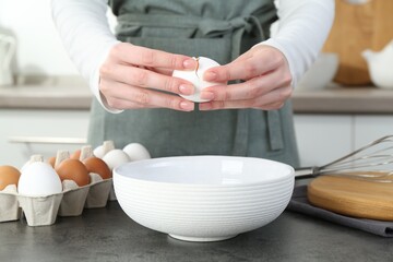 Woman cracking egg into bowl at grey table in kitchen, closeup