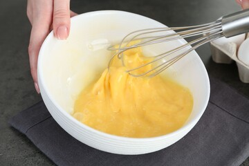 Woman beating eggs with whisk at grey table, closeup