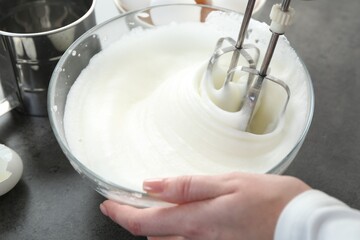 Woman beating egg whites with mixer at grey table, closeup