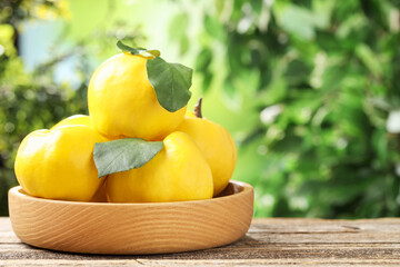 Ripe quinces in bowl on wooden table outdoors, closeup. Space for text
