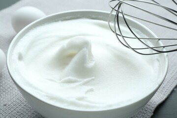Whipped whites in bowl, whisk and eggs on grey table, closeup