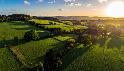 Naklejka premium Golden Hour Aerial View Of Rolling Green Hills And Farmland With Distant Hazy Horizon At Sunset