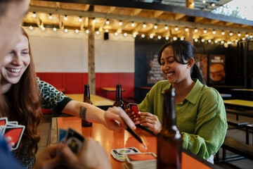 Friends enjoying card game and beer at bar with laughter
