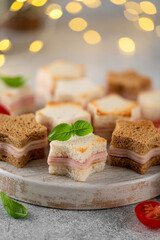 Christmas star shaped cheese and ham mini sandwiches on a wooden board on a gray background. Festive food. Selective focus.