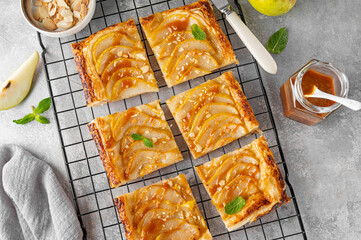 Pear puff pastry pie with caramel sauce and almond on a gray concrete background. Delicious pie.
