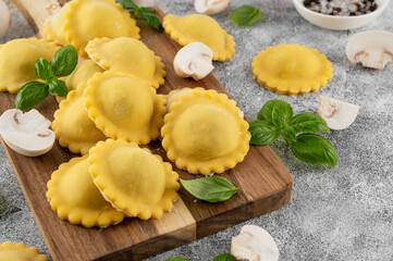 Raw homemade Italian ravioli pasta with ricotta, mushrooms and parmesan cheese on a board on a concrete background. Top view.