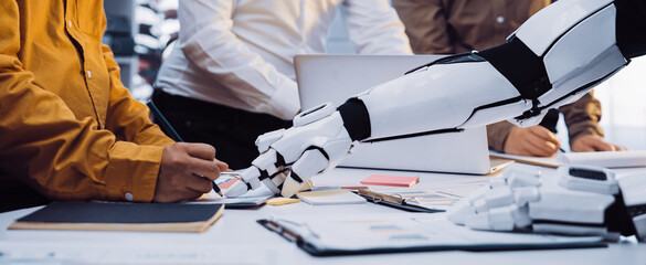 A human and a robotic hand collaborate in a modern office environment. This scene represents the...