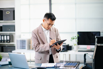 Asian businessman using smartphone and laptop in modern office, symbolizing communication, connection, productivity, and modern corporate success.