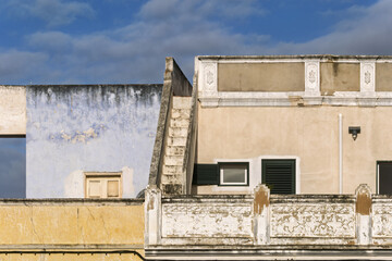Fototapeta premium Weathered building facade with staircase and small windows, and yellow base with ornate white detailing, all showing signs of age in Olhao, Portugal