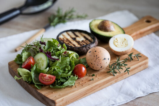 A high-protein, healthy meal arrangement on a wooden cutting board, featuring a small green salad with mixed greens, cherry tomatoes,