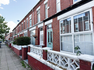 Row of red brick terrace houses in Manchester with pastel doors and decorative white fences